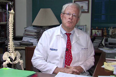 Dr. Nordt seated at his desk in his office, a spine model at his side